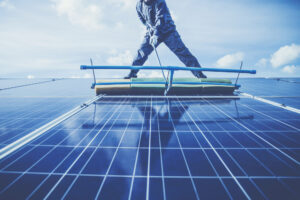 Eine Person reinigt mit einer großen Bürste die Oberfläche einer Photovoltaikanlage.