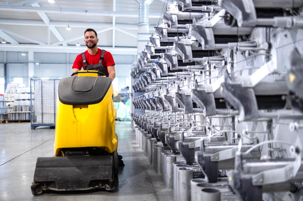 Eine Person fährt mit einer gelben Reinigungsmaschine durch eine Industriehalle.